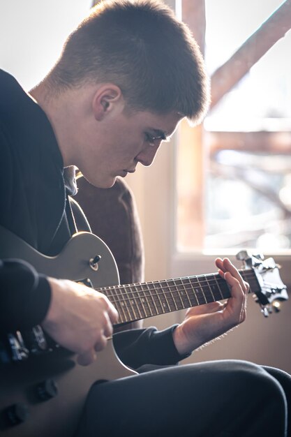 Un joven toca la guitarra eléctrica en su habitación.