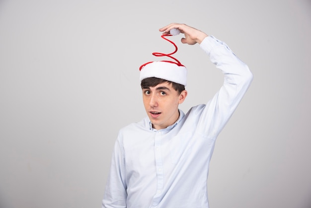 Joven tocando el sombrero rojo de Santa en la pared gris.