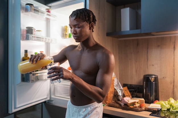 Joven tomando un refrigerio en medio de la noche en casa junto a la nevera