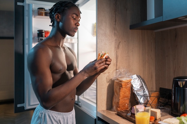 Joven tomando un refrigerio en medio de la noche en casa junto a la nevera