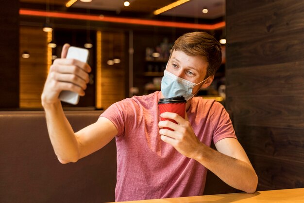 Joven tomando un selfie mientras usa una mascarilla en una cafetería.