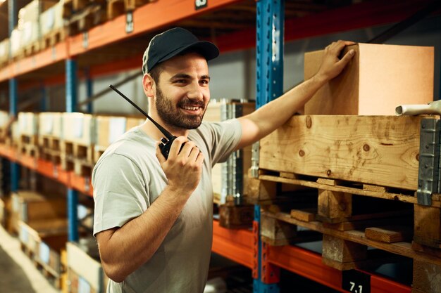 Joven trabajador de almacén que usa walkie talkie mientras trabaja en el compartimento de almacenamiento