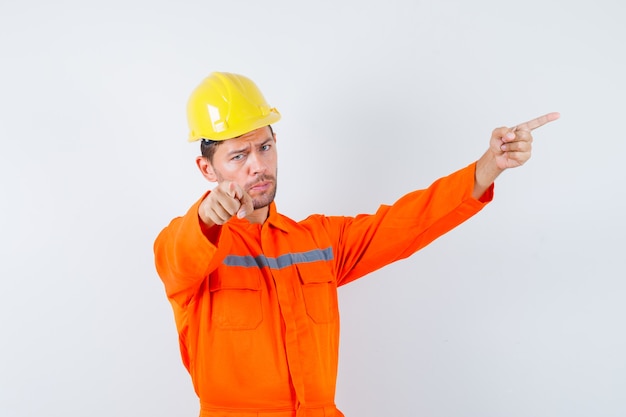 Joven trabajador apuntando a un lado y lejos en uniforme, casco.