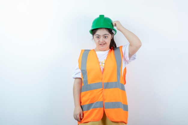 Joven trabajador de la construcción en casco de pie sobre la pared blanca