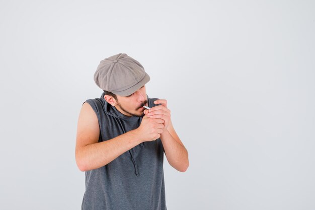 Joven trabajador encendiendo cigarrillos en camiseta gris y gorra y mirando serio