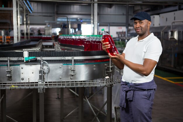 Joven trabajador inspeccionando la botella de jugo en la fábrica.