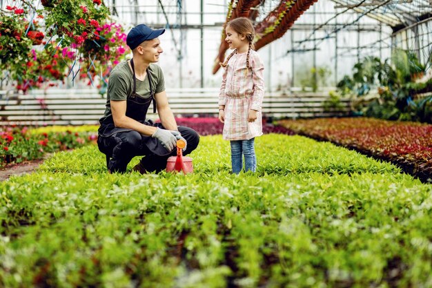 Joven trabajador de invernadero hablando con una niña pequeña mientras nutre plantas