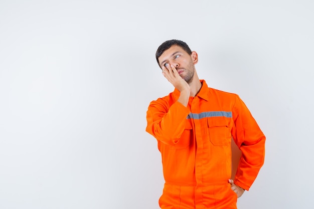 Joven trabajador de la mano en la cara en uniforme y con cara de tristeza.