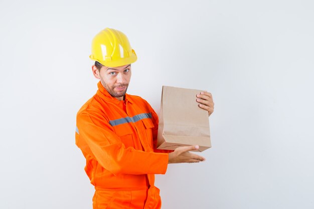 Joven trabajador mostrando bolsa de papel en uniforme