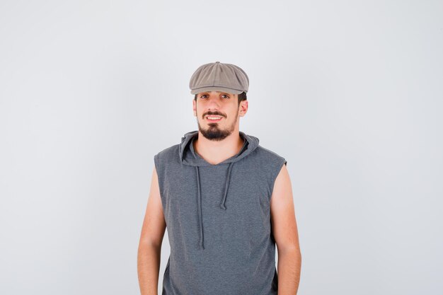 Joven trabajador de pie derecho y sonriendo en camiseta gris y gorra y mirando feliz