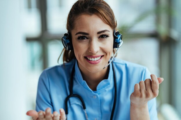 Joven trabajador de la salud feliz usando auriculares y hablando con pacientes mientras trabaja en el centro de llamadas
