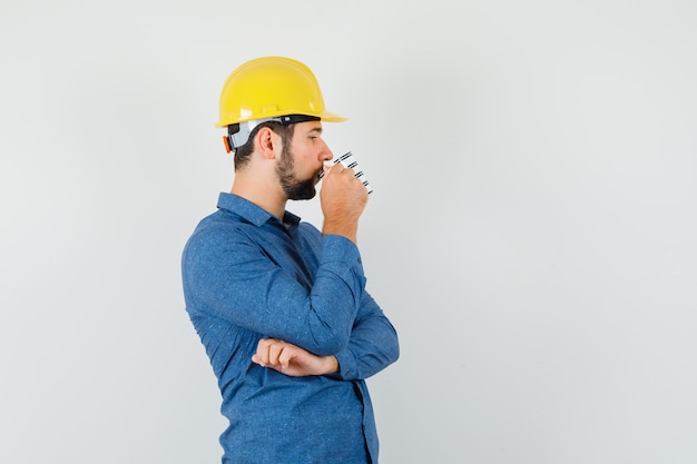 Joven trabajador tomando café mientras piensa en camisa, casco