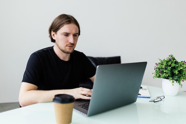 Joven trabajando en casa con laptop y papeles en el escritorio