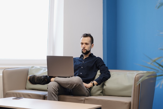 Joven trabajando en la computadora portátil mientras está sentado en el sofá de la oficina