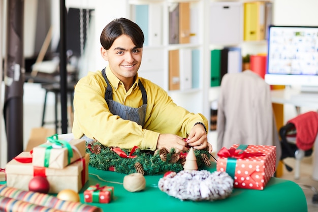 Joven en el trabajo, haciendo una corona de Navidad y envolviendo regalos