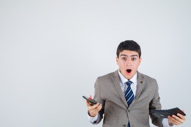 Joven en traje formal sosteniendo teléfono y calculadora y mirando sorprendido