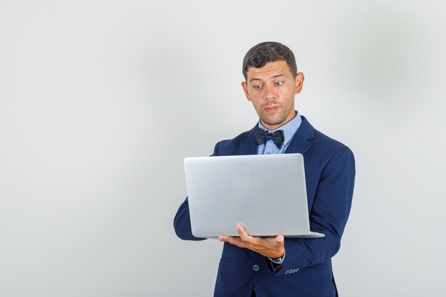 Joven en traje trabajando en equipo portátil y mirando ocupado