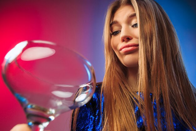 La joven triste en ropa de fiesta posando con una copa de vino.