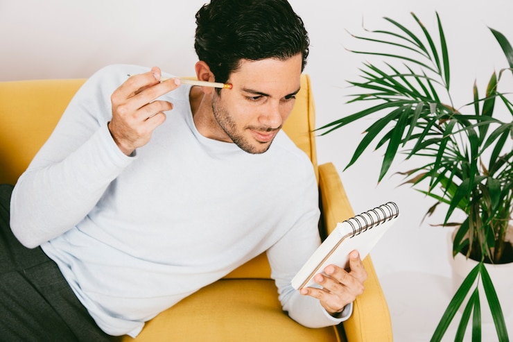 Foto gratuito joven tumbado en el sofá con libreta y bolígrafo