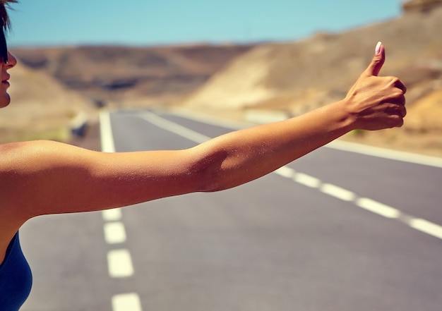 Joven turista caucásico haciendo autostop a lo largo de una carretera en la puesta del sol