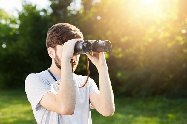 Joven turista explorador mirando a través de binoculares a distancia explorando lugares desconocidos. Viajero mirando a través de binoculares