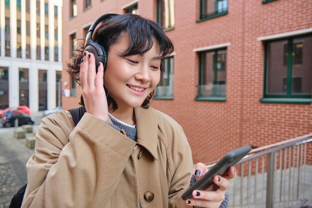 Joven turista feliz escucha música en auriculares bebe comida para llevar y revisa los soportes de teléfonos móviles