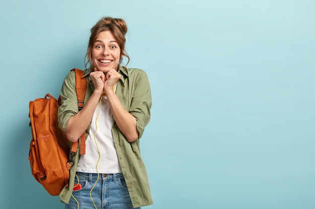 La joven turista llena de alegría tiene una reacción feliz cuando ve algo increíble, mantiene las manos apretadas cerca de la barbilla