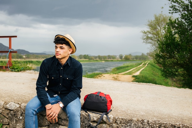 Foto gratuita joven turista llevaba sombrero emplazamiento con mochila en puente