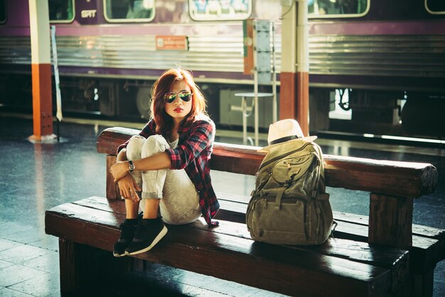 Joven turista mujer moderna con mochila sentado en la estación de tren. Concepto turístico de vacaciones.