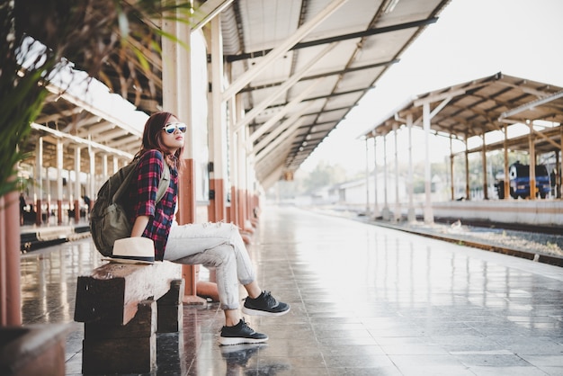 Joven turista mujer moderna con mochila sentado en la estación de tren. Concepto turístico de vacaciones.