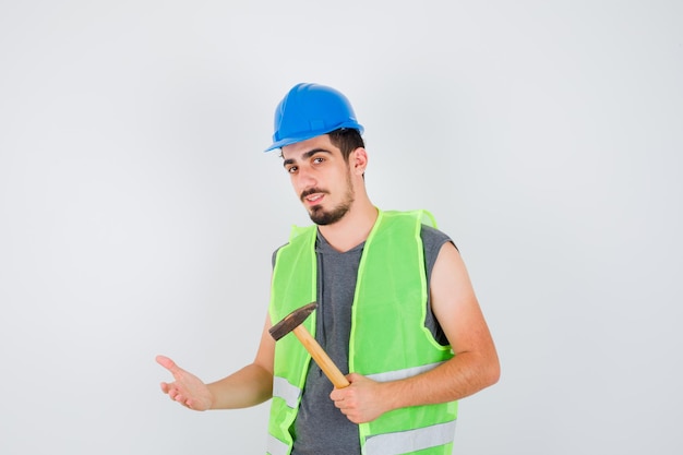 Joven en uniforme de construcción sosteniendo el hacha y estirando la mano hacia él y mirando feliz