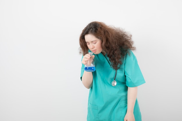 joven en uniforme verde sosteniendo un frasco de vidrio con líquido azul.