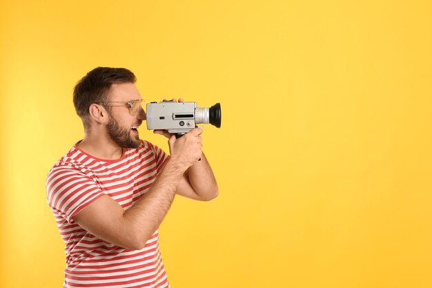 Joven usando una cámara de video vintage en un espacio de fondo amarillo para texto