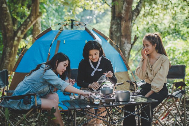 Una joven vertió agua de una botella en un hervidor para hervir para beber café caliente con sus amigas frente a una tienda de campaña en el bosque