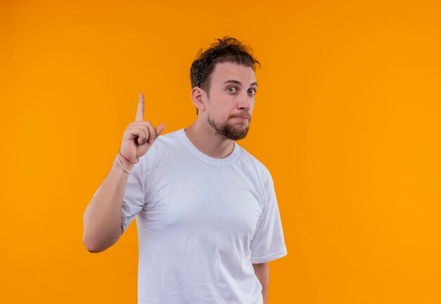 Joven vestido con camiseta blanca apunta hacia arriba en la pared naranja aislada