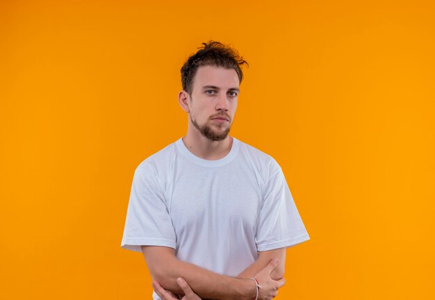 Joven vestido con camiseta blanca cruzando las manos sobre la pared naranja aislada