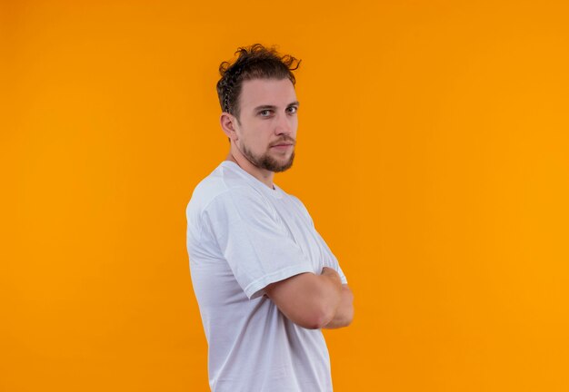 Joven vestido con camiseta blanca cruzando las manos sobre la pared naranja aislada