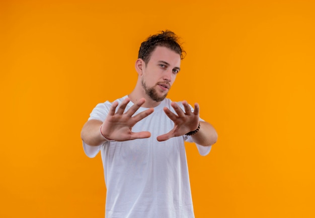 Joven vestido con camiseta blanca mostrando gesto de parada en pared naranja aislada