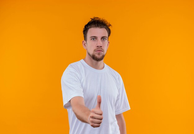 Joven vestido con camiseta blanca con el pulgar hacia arriba en la pared naranja aislada