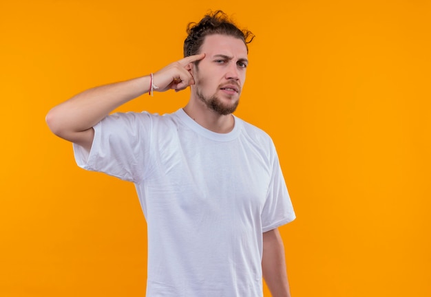 Joven vestido con camiseta blanca puso su dedo en la frente en la pared naranja aislada