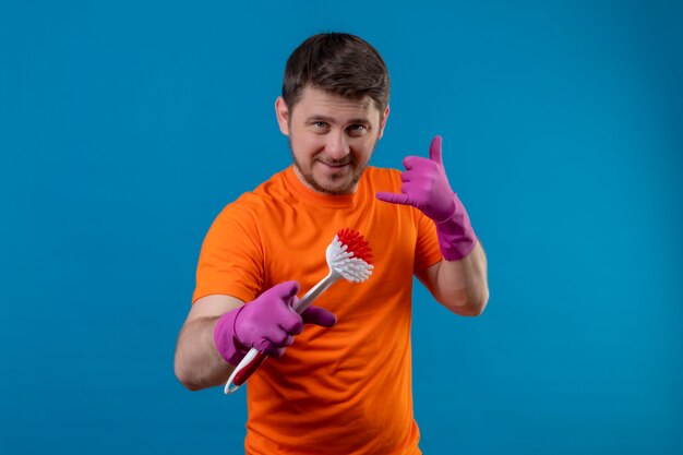 Joven vestido con camiseta naranja y guantes de goma con cepillo para fregar