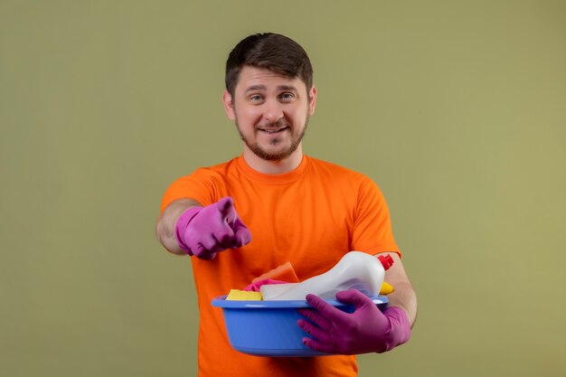 Joven vestido con camiseta naranja y guantes de goma con lavabo con herramientas de limpieza