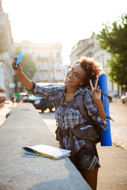 Joven viajero africano hermosa mujer con mochila sonriendo, haciendo selfie.