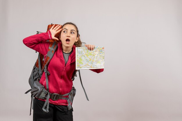 Joven viajero sorprendido con mochila grande sosteniendo mapa en gris