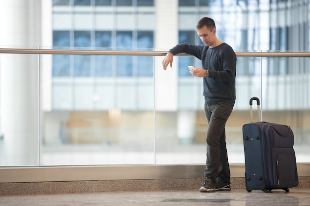 Joven viajero utilizando teléfono inteligente en el aeropuerto