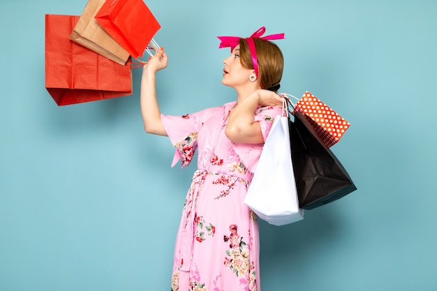 Una joven de vista frontal en vestido rosa diseñado con flores posando sosteniendo paquetes de compras en azul