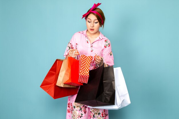 Una joven de vista frontal en vestido rosa diseñado con flores posando sosteniendo paquetes de compras en azul