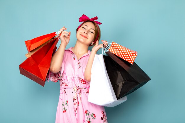 Una joven de vista frontal en vestido rosa diseñado con flores posando sosteniendo paquetes de compras en azul