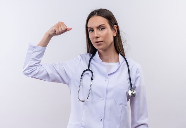 Joven vistiendo bata médica estetoscopio haciendo gesto fuerte en la pared blanca aislada