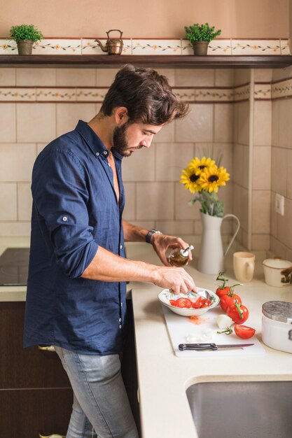 Joven vistiendo la ensalada con aceite de oliva en la cocina